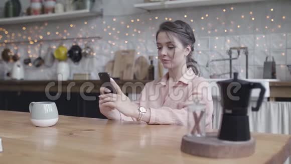 年轻的女人坐在家里的厨房桌子旁用智能手机做她的小生意库存数据视频的预览图