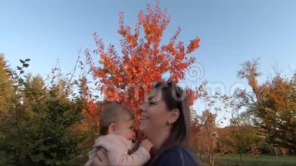 一边看着幸福的年轻母亲手里拿着女婴用爱看着她秋天的照片视频的预览图