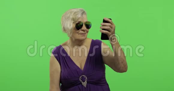 一位老年妇女在智能手机上拍照赛尔夫铬键视频的预览图