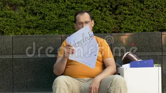 街上的失业男子带着刻字的科顿需要工作被解雇的人坐在一条水泥街上视频的预览图