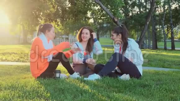 三个朋友在晨跑后坐在草地上他们笑着说话视频的预览图