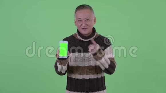 快乐成熟的日本男人展示电话和大拇指视频的预览图