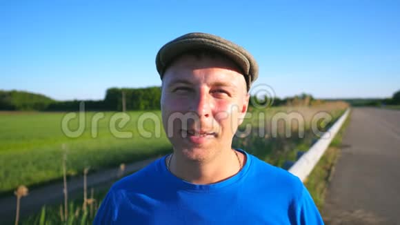成年微笑男子站在草地背景的肖像戴帽子的无忧无虑的家伙用窄窄的镜头视频的预览图
