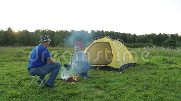 晚上一男一女在靠近火堆的帐篷旁做晚饭视频的预览图