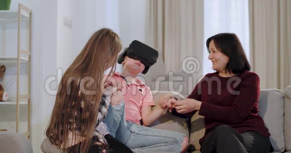 美丽的老奶奶和她的孙子们在一起玩得很开心孙子用虚拟现实眼镜玩视频的预览图