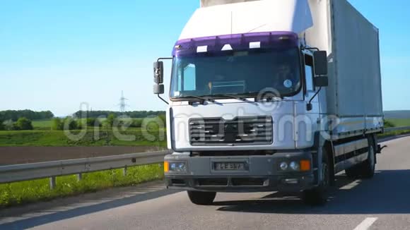 摄像机跟随卡车货物拖车在公路上行驶并在夏季运输货物卡车驶过视频的预览图
