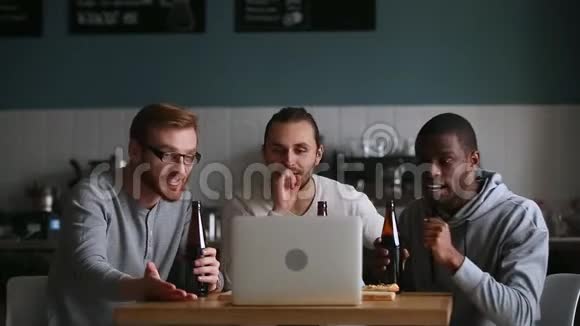 不同的朋友在酒吧闲逛在笔记本电脑上观看在线比赛视频的预览图