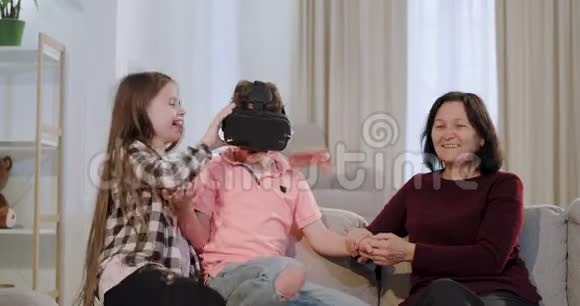 在客厅里祖母和她的孙子们玩得很开心孙子用虚拟现实眼镜玩视频的预览图