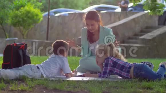 小男孩和女孩听着女孩子读着迷人的书坐在阳光明媚的户外草坪上视频的预览图