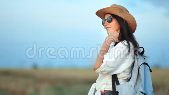 戴着帽子和太阳镜的轻松美丽的旅行背包客妇女在日落时享受大自然的美丽视频的预览图