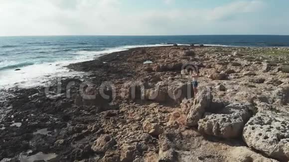 站在岩石上拍摄波浪海照片的女性鸟瞰图强烈的海浪撞击海岸女人拿着相机视频的预览图