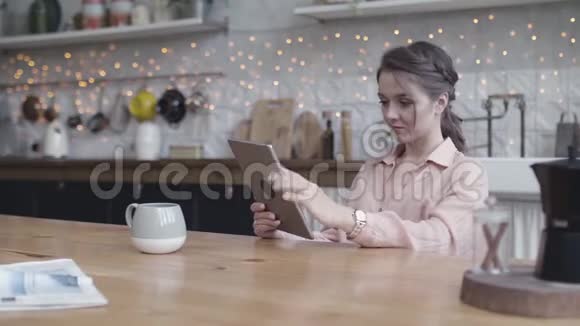 年轻女子坐在家里的餐桌旁用一台数码平板电脑做她的小生意库存数据视频的预览图