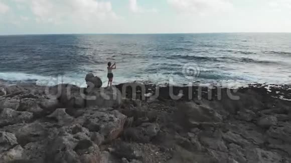 年轻的女性站在海边的大岩石上拍照海浪很大一名年轻女子在反渗透飞机上用相机拍摄的无人机视频的预览图