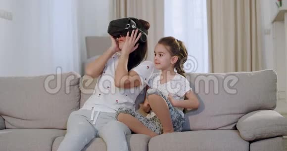 一个可爱的小女孩和她成熟的母亲一起用一种新技术在沙发上探索虚拟世界视频的预览图