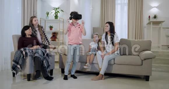 成熟的母亲带着她的三个孩子和一个奶奶坐在客厅的沙发上玩虚拟现实视频的预览图