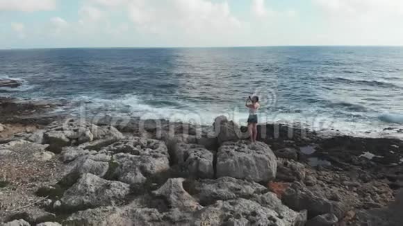 白种人妇女站在悬崖上用相机手机拍摄海平线的照片强烈的波浪撞击海滩波浪视频的预览图