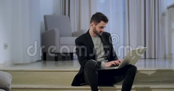 一个心情好的商人坐在客厅的楼梯上在家里的笔记本上工作视频的预览图