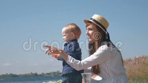 快乐的母亲微笑的快乐的母亲在帽子和小男孩享受户外和看湖视频的预览图