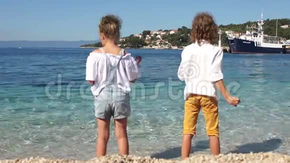 哥哥姐姐同学们在克罗地亚小镇和大海的背景下在清澈湛蓝的海水里扔石头视频的预览图