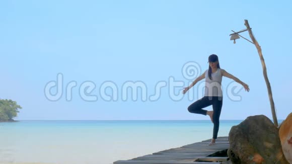 4K暑假期间一个女人站在一条腿上在海上的木桥上练习瑜伽亚洲年轻迷人视频的预览图