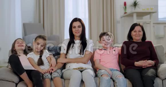有魅力的女人带着白色的微笑她的三个孩子和奶奶一起看电视坐在上面视频的预览图