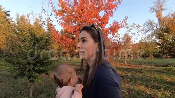 一边看着幸福的年轻母亲手里拿着女婴用爱看着她秋天的照片视频的预览图