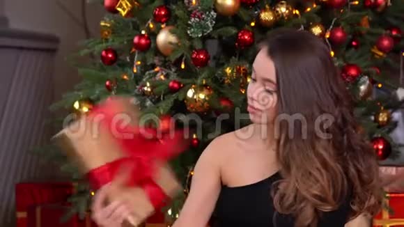 美丽的少女捧着礼物微笑坐在家中的圣诞树旁视频的预览图