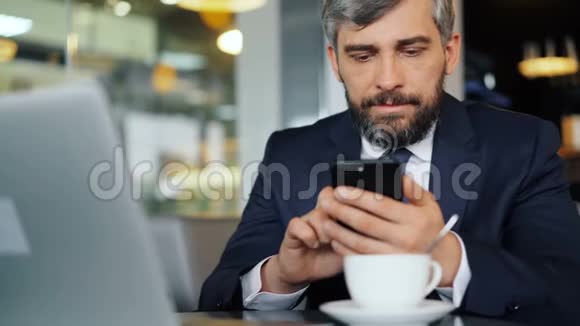 咖啡厅休息时穿着智能手机的有胡子的上班族视频的预览图