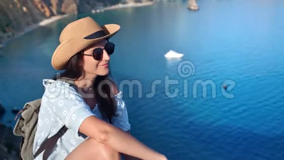 微笑着旅行的女人戴着帽子戴着太阳镜在山景周围欣赏大海视频的预览图