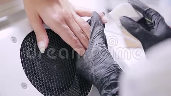 在美容院戴手套的女美甲师在涂胶前给顾客涂指甲油视频的预览图