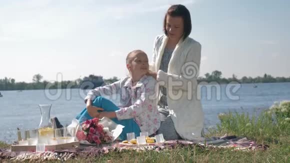 快乐的家庭快乐的母亲编织着孩子的头发在草坪上野餐时放松交流视频的预览图