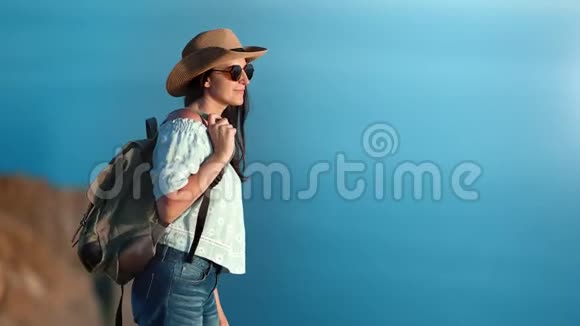 愉快的旅行沉思的女人戴着帽子太阳镜从山上看到令人惊叹的海洋景观视频的预览图