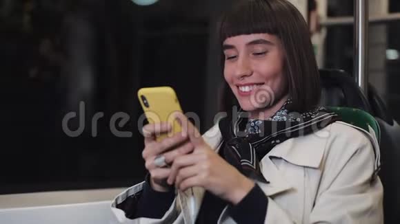 微笑的年轻女子在公共交通上看智能手机上的视频晚上特写镜头城市灯光背景视频的预览图