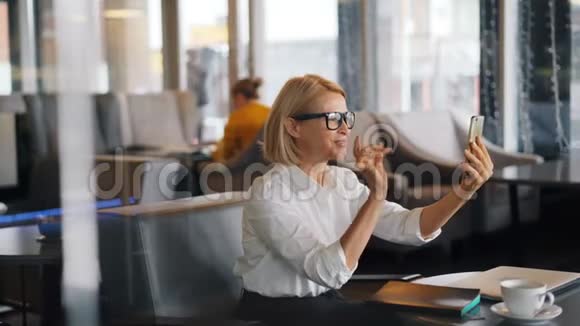优雅成熟的金发女郎在智能手机上聊天在咖啡馆打视频电话视频的预览图