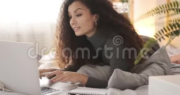 在床上使用笔记本电脑和书写笔记的女人视频的预览图
