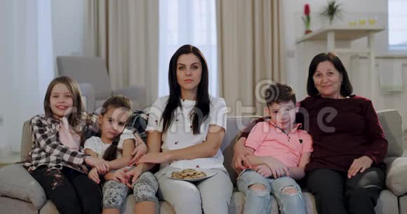 集中和有趣的家庭奶奶和她美丽的女儿和孙子在电视上看喜剧电影视频的预览图
