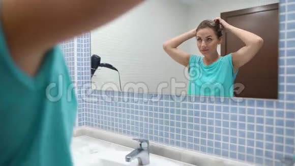 漂亮的女人在浴室镜子前把头发和发型分开视频的预览图