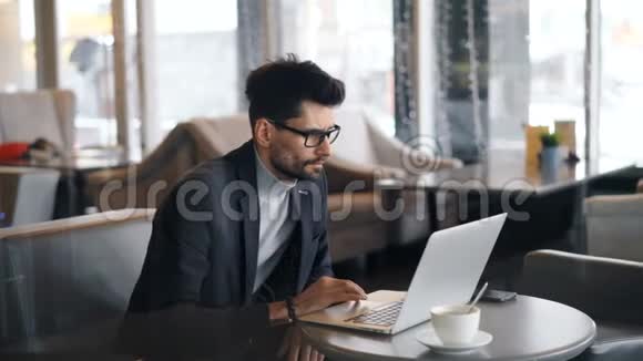 在咖啡馆工作的男性自由职业者用手提电脑看屏幕触摸键盘视频的预览图