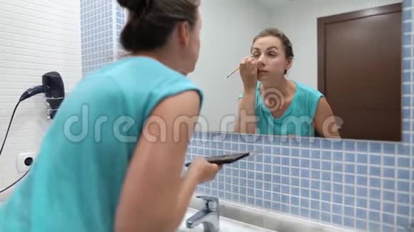 漂亮的女人在浴室镜子前用眼影和化妆刷做眼妆视频的预览图