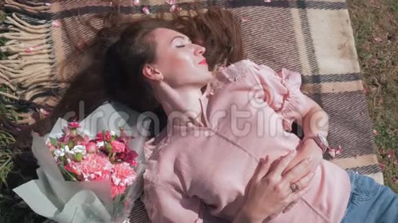 快乐可爱的女人躺在草坪上床罩上美丽的花束旁享受户外娱乐顶景视频的预览图
