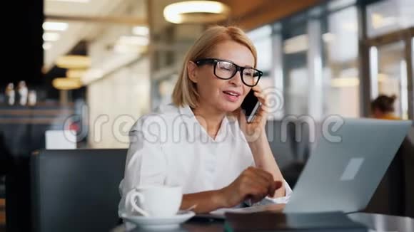 开朗的女企业家在咖啡馆里用手机说话视频的预览图