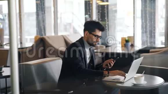 在咖啡馆工作的企业主使用笔记本电脑和智能手机视频的预览图