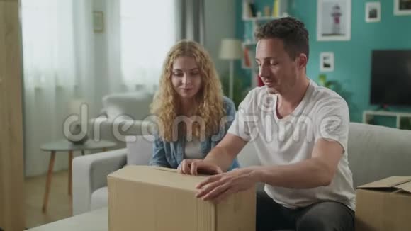 幸福的一对夫妇坐在客厅的沙发上打开拆开纸箱包裹视频的预览图