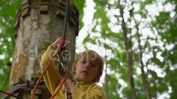 一个穿着安全装备的小男孩在森林探险公园的树梢上骑着高空滑索他爬上了高高的绳索视频的预览图