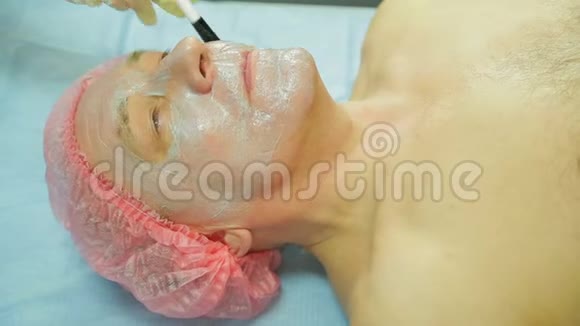 戴手套的女性美容师用海草面具涂在男人的脸上侧视图视频的预览图
