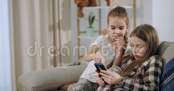 特写魅力和美丽的两个姐妹一起玩游戏使用智能手机而坐在沙发上视频的预览图