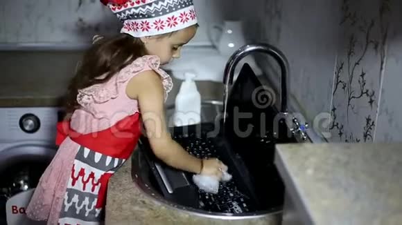小女孩在厨房的水槽里洗手提电脑穿着红色围裙视频的预览图