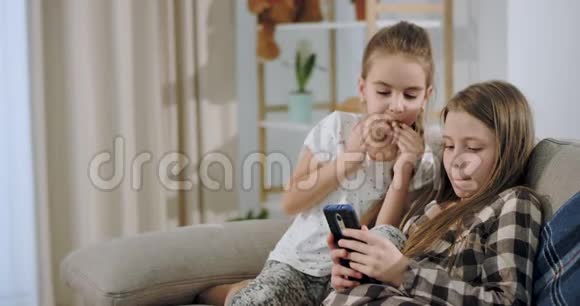 很有吸引力的两个姐妹在放学后坐在沙发上玩智能手机游戏放松一下视频的预览图