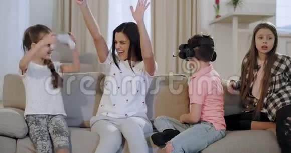 美丽的微笑的母亲她的三个孩子坐在电视前的沙发上在PSP上玩他们非常喜欢视频的预览图