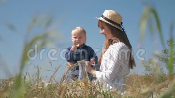 可爱的小男孩在家庭野餐时吃柠檬和鬼脸在大自然中坐在母亲的怀里紧紧地坐在草地上视频的预览图
